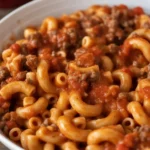 A bowl of hearty goulash featuring ground beef, pasta, and rich tomato sauce.