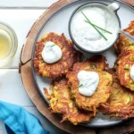 Crispy Zucchini Fritters topped with fresh garden herbs and served with herbed sour cream sauce.