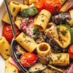 A bowl of roasted veggie pasta with colorful roasted vegetables and herbs on top.
